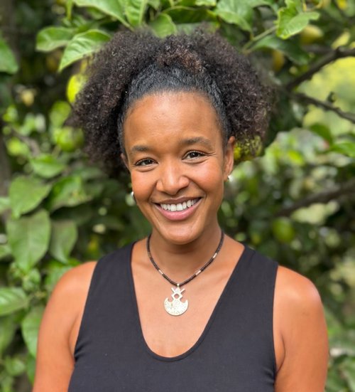 Portrait of Aïcha Cissé smiling outdoors among green leaves